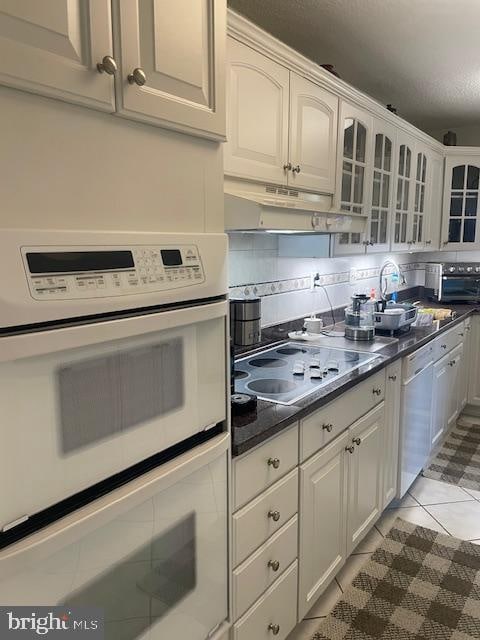 kitchen with stainless steel dishwasher, tasteful backsplash, white cabinetry, and white double oven