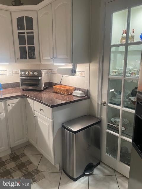 kitchen featuring light tile patterned floors, dark stone counters, white cabinets, and decorative backsplash