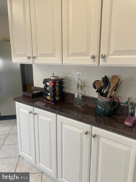 bar with dark stone counters, white cabinetry, and light tile patterned flooring