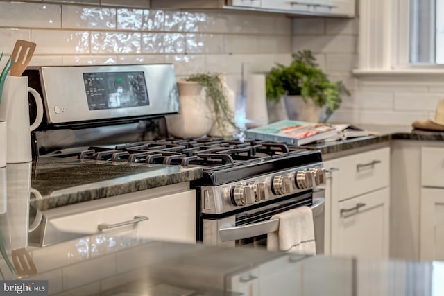 kitchen featuring white cabinetry, dark stone countertops, stainless steel range with gas cooktop, and backsplash