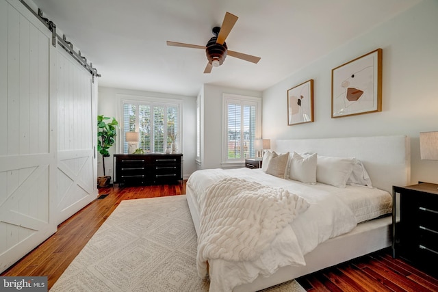 bedroom with a barn door, dark hardwood / wood-style floors, and ceiling fan