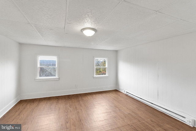 unfurnished room featuring hardwood / wood-style floors, a paneled ceiling, wooden walls, and a baseboard heating unit