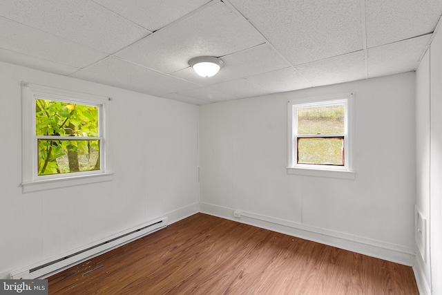 empty room with hardwood / wood-style floors, a baseboard radiator, and a paneled ceiling