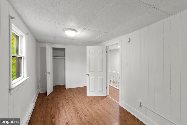 unfurnished bedroom featuring wood walls, a drop ceiling, hardwood / wood-style flooring, and a closet