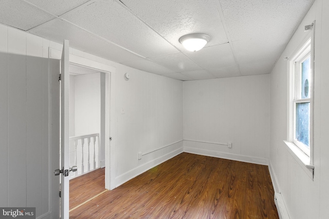 unfurnished room with baseboard heating, a paneled ceiling, and wood-type flooring