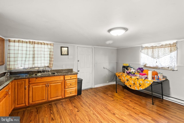 kitchen featuring light wood-type flooring, sink, crown molding, and dark stone countertops