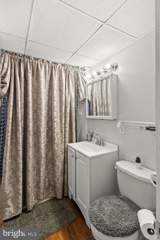 bathroom with a paneled ceiling, curtained shower, wood-type flooring, vanity, and toilet