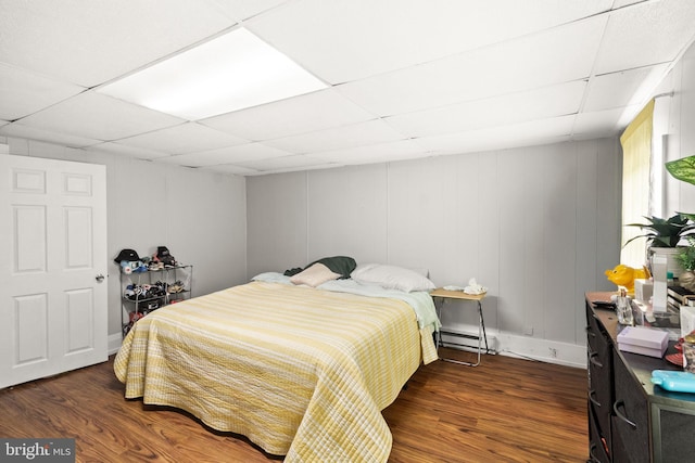 bedroom with a baseboard radiator, dark hardwood / wood-style flooring, and a paneled ceiling