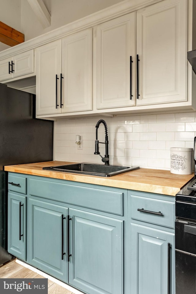 kitchen featuring light wood-type flooring, tasteful backsplash, sink, white cabinets, and butcher block countertops