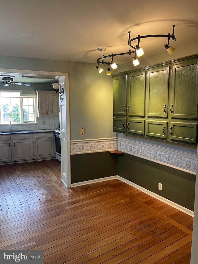 kitchen with decorative backsplash, stove, sink, hardwood / wood-style floors, and green cabinets