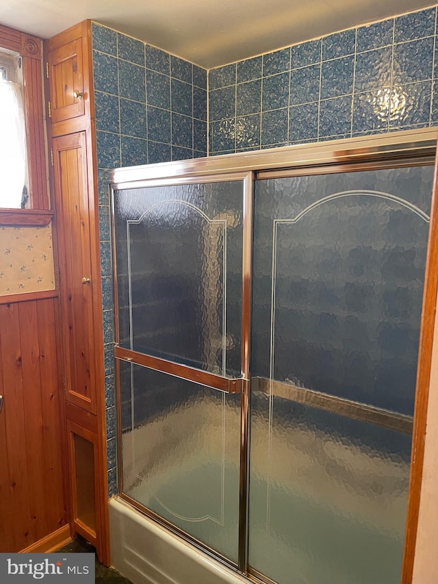 bathroom featuring wood walls and bath / shower combo with glass door