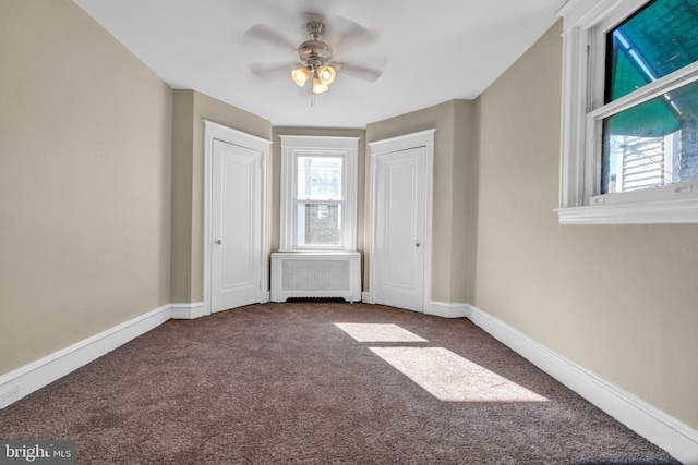 unfurnished bedroom featuring radiator, ceiling fan, multiple windows, and carpet flooring