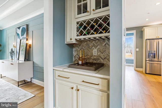 bar with light stone counters, white cabinets, tasteful backsplash, light hardwood / wood-style flooring, and stainless steel fridge