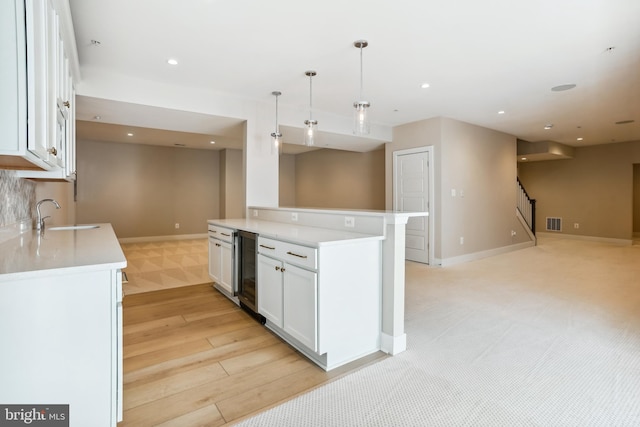 kitchen with light wood-type flooring, pendant lighting, sink, white cabinets, and beverage cooler