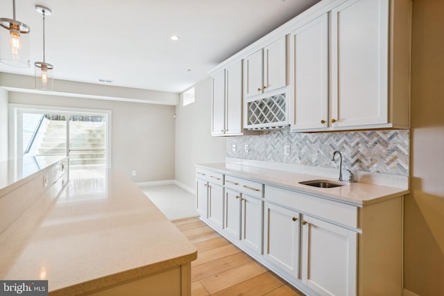 kitchen featuring light hardwood / wood-style flooring, pendant lighting, sink, and white cabinets