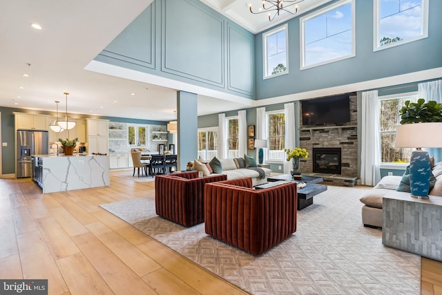 living room featuring sink, a fireplace, a towering ceiling, light hardwood / wood-style flooring, and a notable chandelier