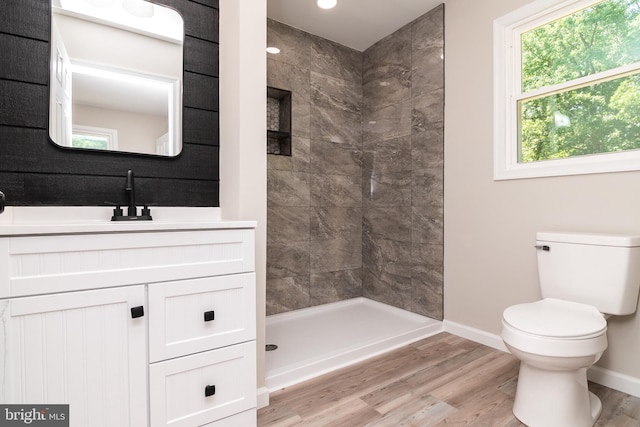 bathroom with toilet, vanity, wood-type flooring, and a tile shower