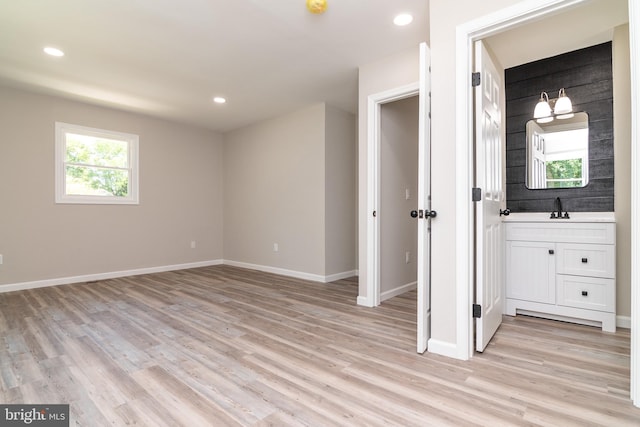 unfurnished bedroom with ensuite bath, sink, and light wood-type flooring