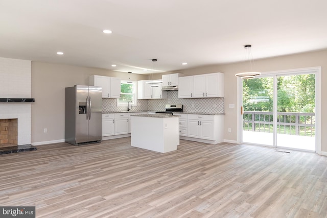 kitchen with white cabinets, a kitchen island, pendant lighting, light wood-type flooring, and appliances with stainless steel finishes