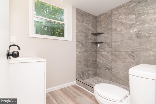 bathroom featuring wood-type flooring, vanity, toilet, and tiled shower