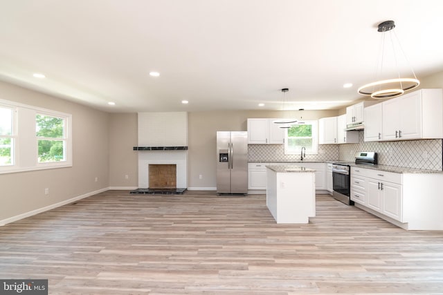 kitchen featuring stainless steel appliances, white cabinets, decorative light fixtures, and light wood-type flooring