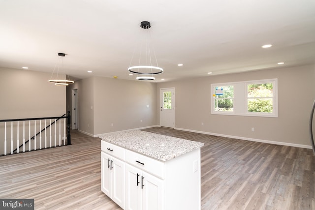 kitchen with light hardwood / wood-style floors, light stone counters, hanging light fixtures, a kitchen island, and white cabinets