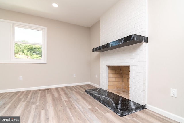 unfurnished living room featuring a brick fireplace and light wood-type flooring