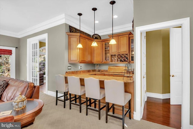 kitchen featuring ornamental molding, light wood-type flooring, decorative light fixtures, light stone countertops, and a kitchen breakfast bar