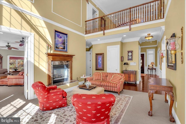 living room with ornamental molding, a towering ceiling, hardwood / wood-style floors, a premium fireplace, and ceiling fan