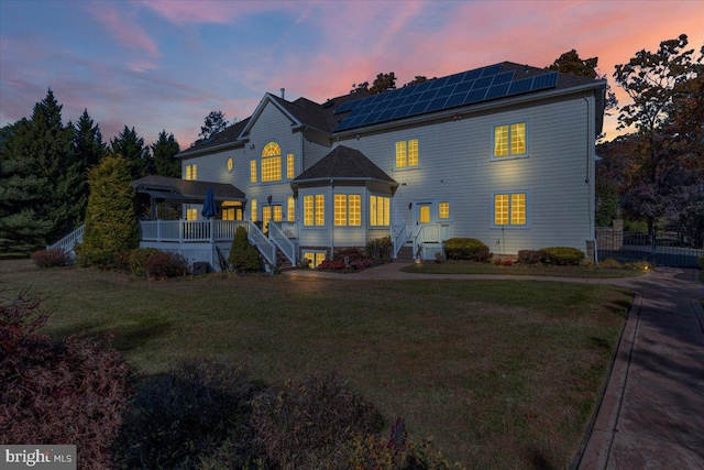 back house at dusk featuring a lawn and a wooden deck