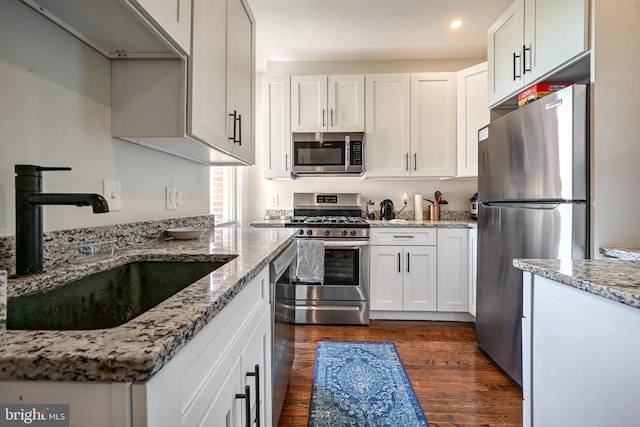 kitchen featuring light stone countertops, white cabinetry, sink, dark wood-type flooring, and appliances with stainless steel finishes