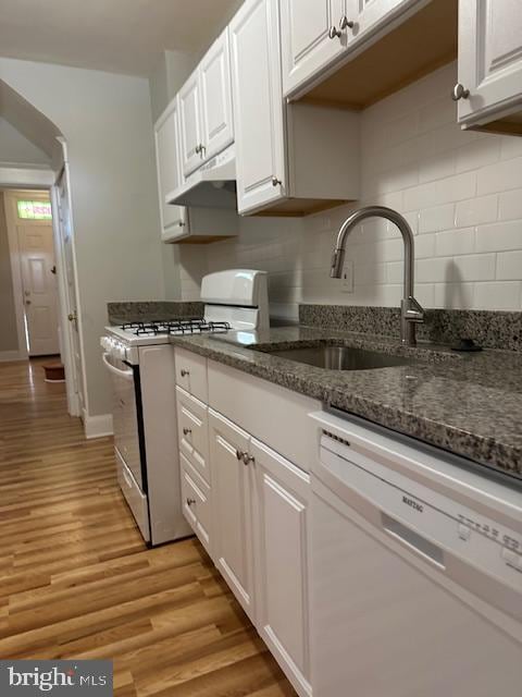 kitchen with white cabinetry, stainless steel gas range, white dishwasher, dark stone countertops, and light hardwood / wood-style flooring