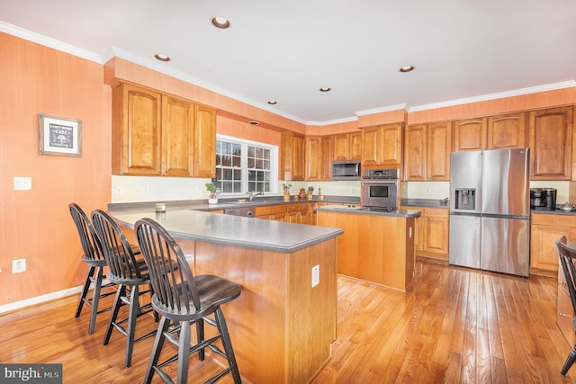 kitchen featuring a kitchen breakfast bar, ornamental molding, stainless steel appliances, light hardwood / wood-style floors, and a kitchen island