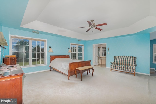 bedroom featuring a tray ceiling, carpet floors, ensuite bathroom, and ceiling fan