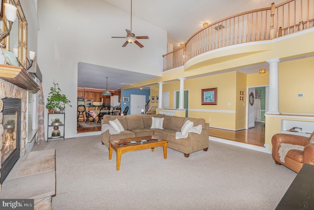 carpeted living room featuring ceiling fan, ornate columns, a fireplace, and a high ceiling