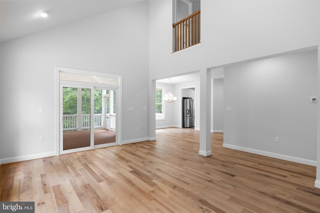 unfurnished living room with high vaulted ceiling, an inviting chandelier, and light hardwood / wood-style flooring