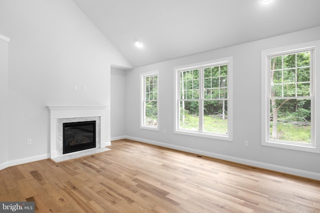 unfurnished living room featuring high vaulted ceiling, light wood-type flooring, and a high end fireplace