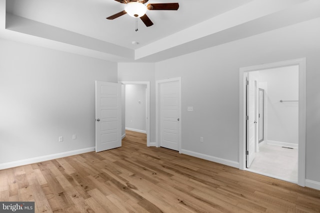 unfurnished bedroom featuring light wood-type flooring, a raised ceiling, ceiling fan, and ensuite bathroom