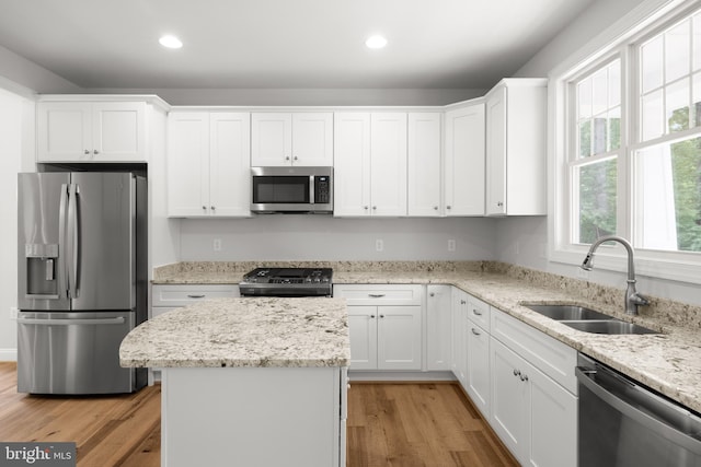 kitchen featuring light stone counters, stainless steel appliances, white cabinetry, sink, and light hardwood / wood-style flooring