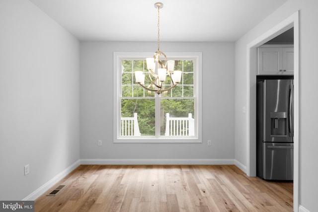 unfurnished dining area featuring an inviting chandelier and light hardwood / wood-style flooring