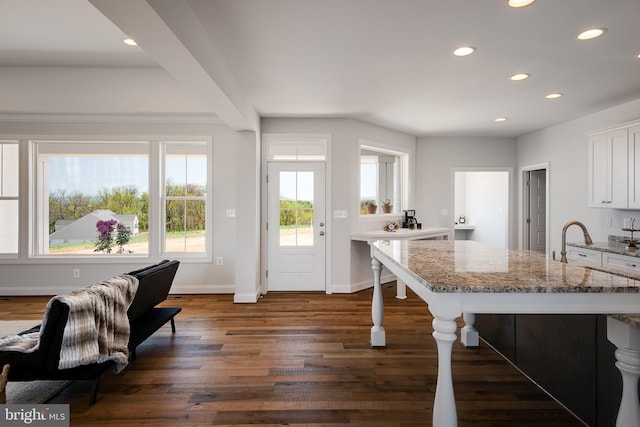 kitchen featuring dark wood-type flooring, light stone counters, a breakfast bar, and white cabinets