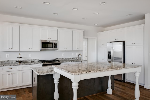 kitchen with white cabinetry, appliances with stainless steel finishes, light stone countertops, a kitchen island with sink, and dark wood-type flooring