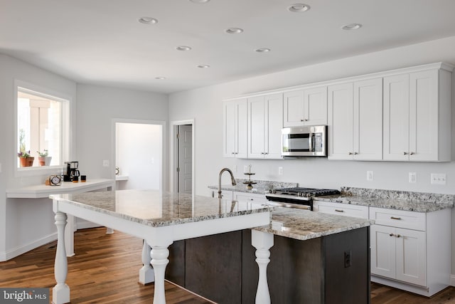 kitchen with an island with sink, dark hardwood / wood-style floors, white cabinetry, and appliances with stainless steel finishes