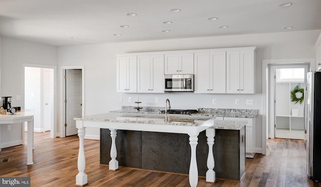 kitchen featuring white cabinetry, light stone counters, a center island with sink, and stainless steel appliances