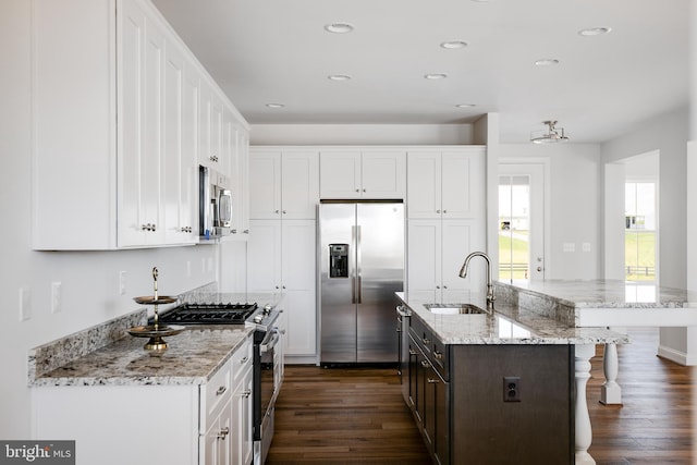 kitchen with appliances with stainless steel finishes, dark hardwood / wood-style flooring, light stone countertops, sink, and an island with sink