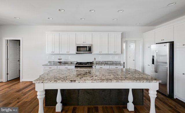 kitchen with dark hardwood / wood-style flooring, light stone counters, white cabinets, an island with sink, and appliances with stainless steel finishes