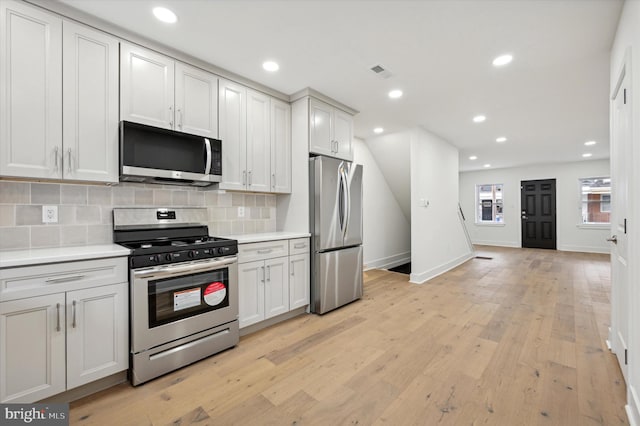 kitchen with backsplash, light hardwood / wood-style floors, white cabinetry, and stainless steel appliances