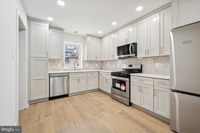 kitchen featuring sink, hanging light fixtures, stainless steel appliances, light hardwood / wood-style floors, and white cabinets