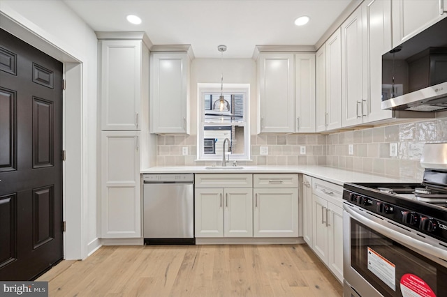 kitchen with appliances with stainless steel finishes, sink, pendant lighting, white cabinets, and light hardwood / wood-style floors