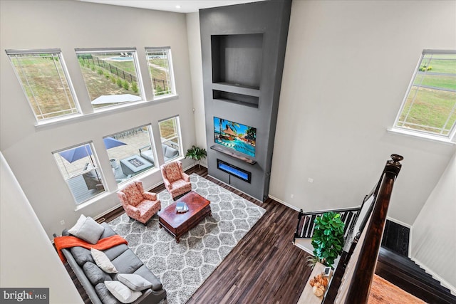 living room with a large fireplace, dark hardwood / wood-style flooring, and a towering ceiling